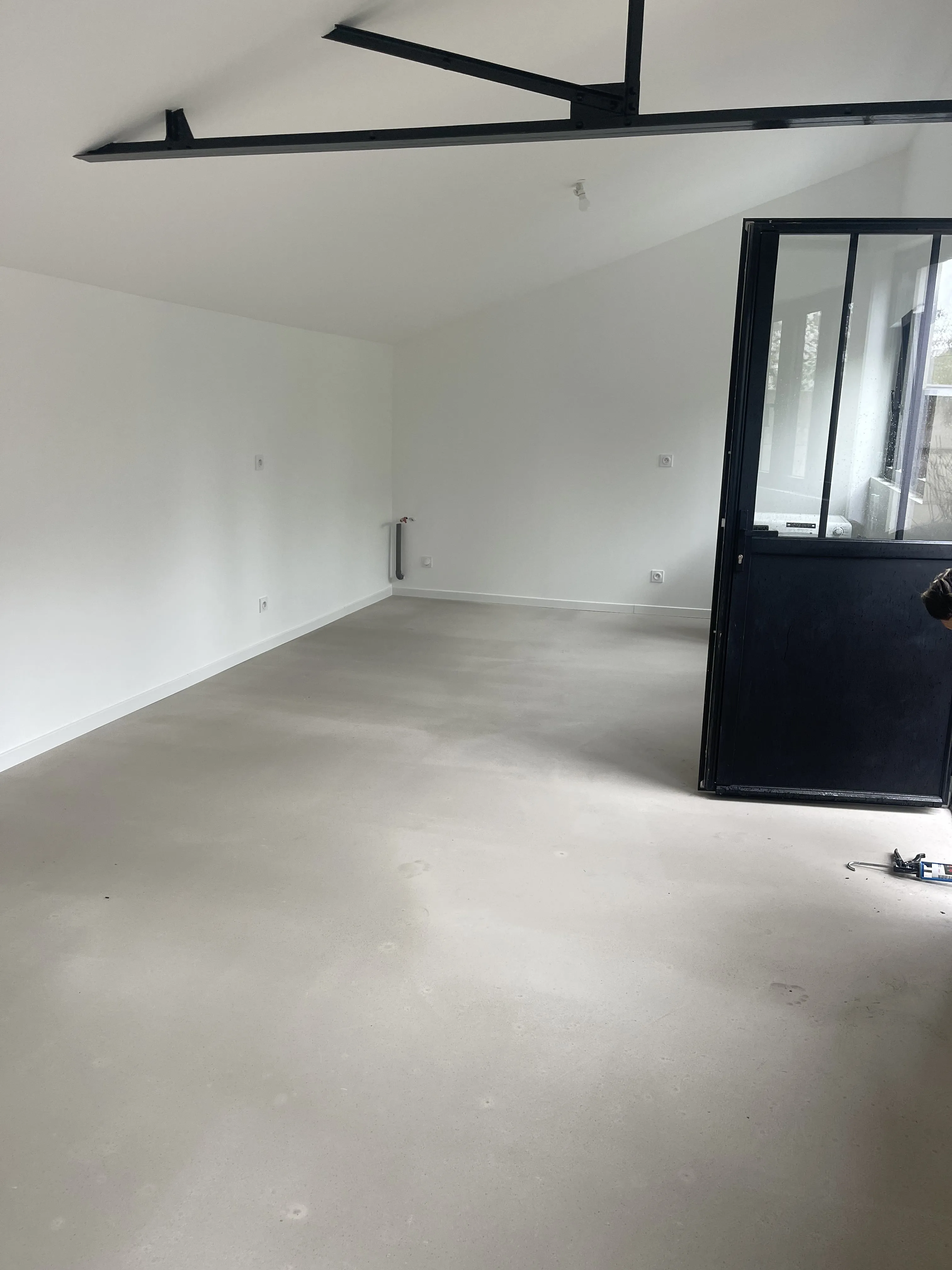 Atelier rénové : murs blancs, sol béton lissé et porte acier vitrée